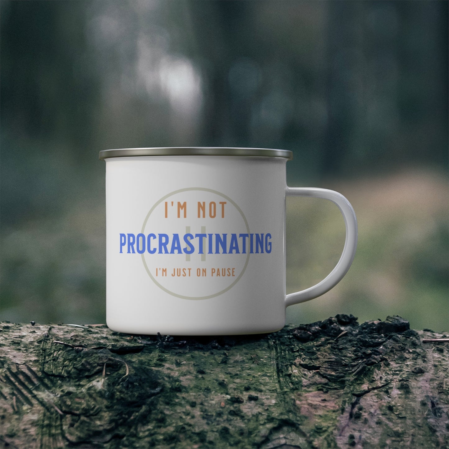 A Printify Funny Procrastination Enamel Camping Mug featuring the phrase Im not procrastinating, Im just on pause rests on a mossy log with a forest backdrop, offering outdoor enthusiasts an ideal moment of reflection in blue and beige tones.