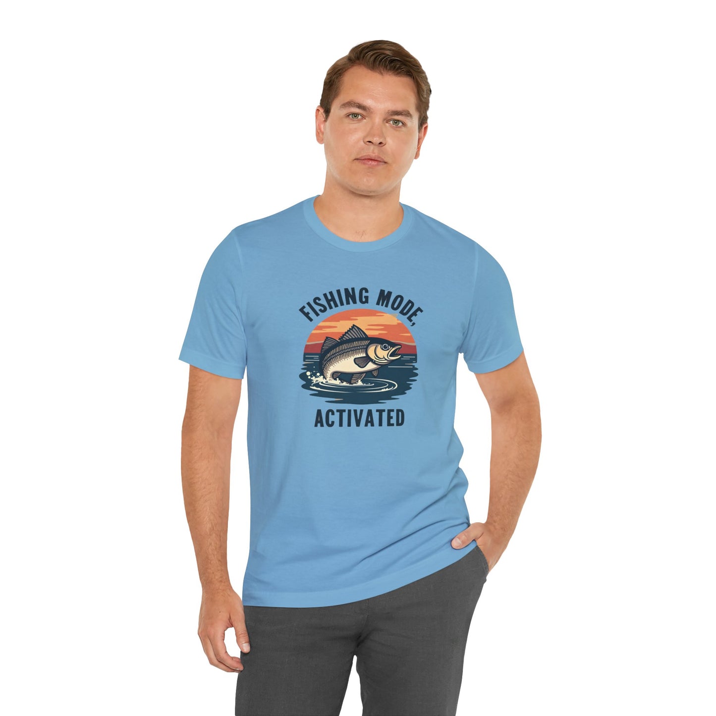 A person in a Printify Fishing Mode Activated Unisex Jersey Short Sleeve T-Shirt stands against a white background. The tee, crafted from soft Airlume cotton, features a light blue design with water and fish graphics. One hand is casually in their pocket.