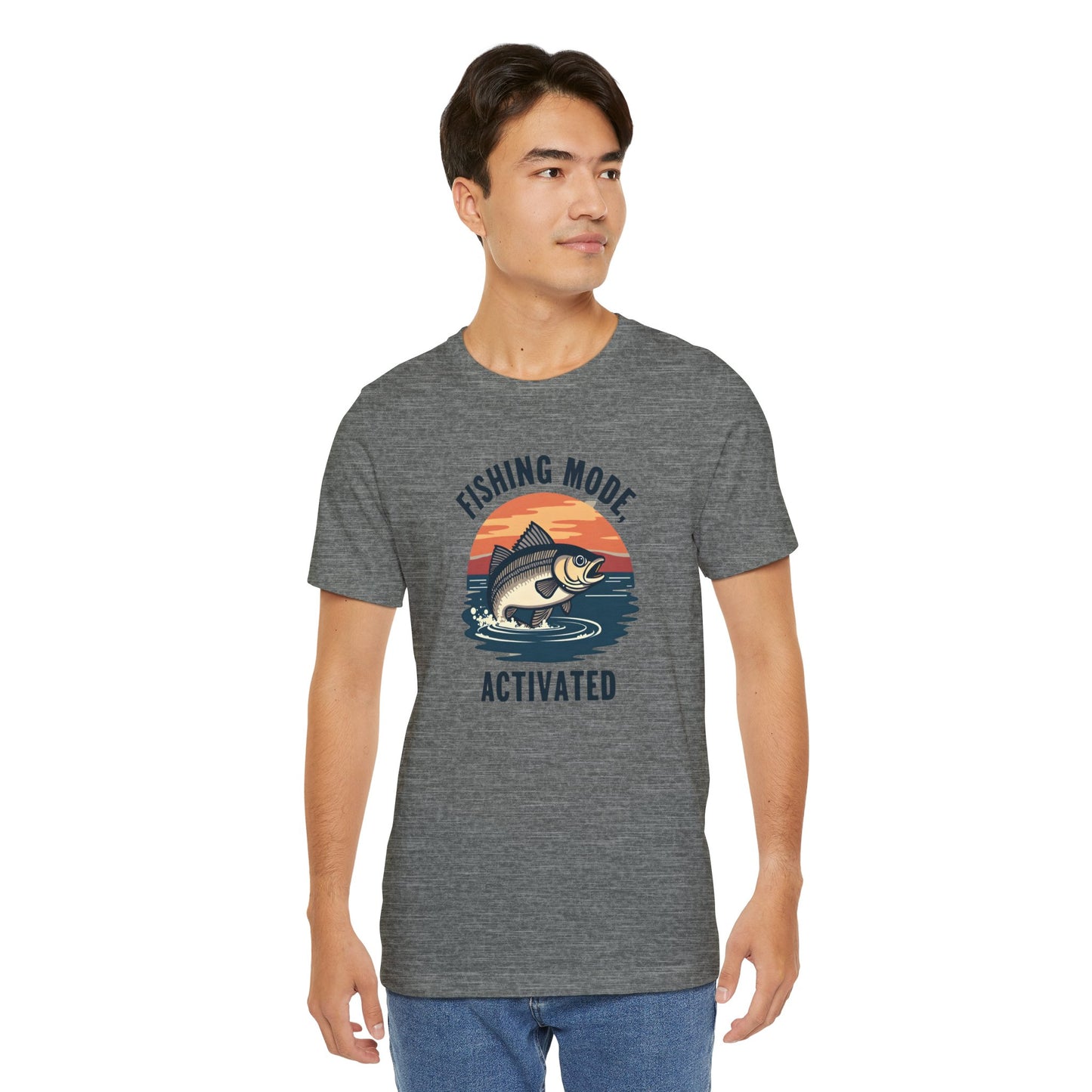 A person models the Fishing Mode Activated Tee for Anglers by Printify, featuring a fish and sunset design on a gray unisex jersey short sleeve T-shirt made from soft Airlume cotton, offering style and comfort against a plain white background.