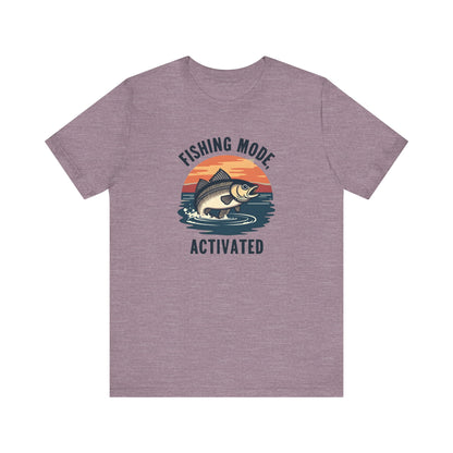 Printifys unisex Fishing Mode Activated gray tee showcases a fish leaping from water against a sunset, crafted from Airlume cotton for comfort on your angling adventures.