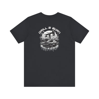 Printifys Vintage Car Graphic Unisex Tee features a black fabric adorned with the bold DRILL & BURN text and a graphic of an oil pump, car, and industrial buildings. The breathable material enhances comfort while the white design offers striking contrast for a captivating casual look.