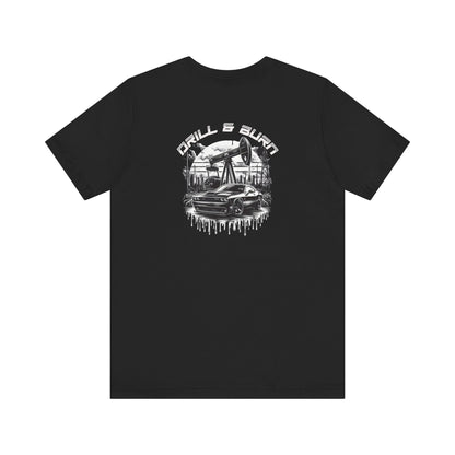 Black Drill & Burn Graphic Unisex Jersey Tee is shown from the front, highlighting an oil drilling scene with a Dodge Challenger doing a burnout. 
